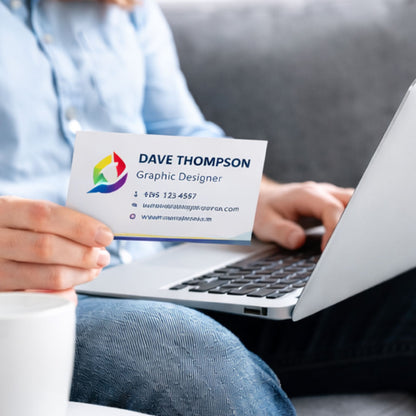 Person holding a business card with 'Dave Thompson' and 'Graphic Designer' details, sitting in front of a laptop.