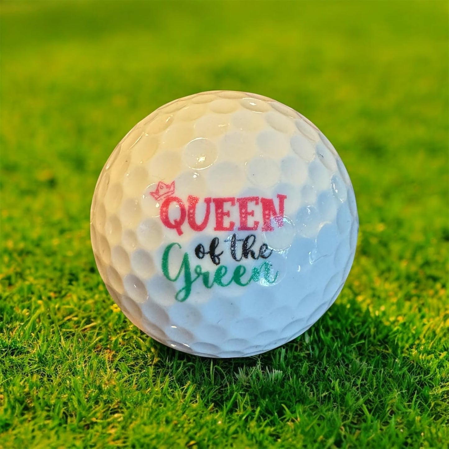 Golf ball with 'Queen of the Green' text on a grassy background