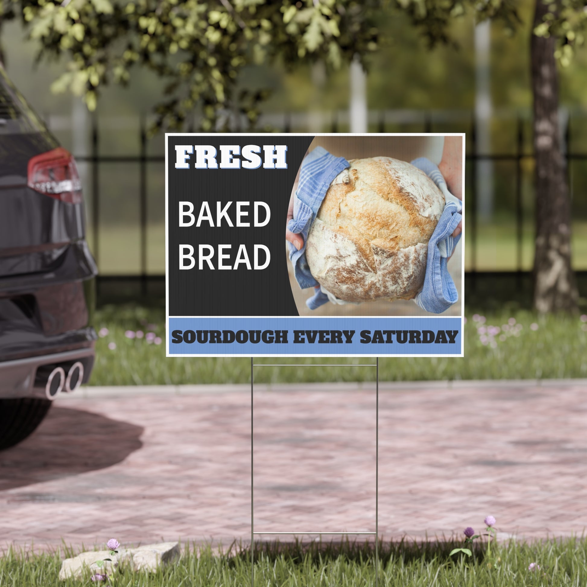 Promotional square sign for fresh baked bread with a loaf of bread and gloved hands, placed outdoors.